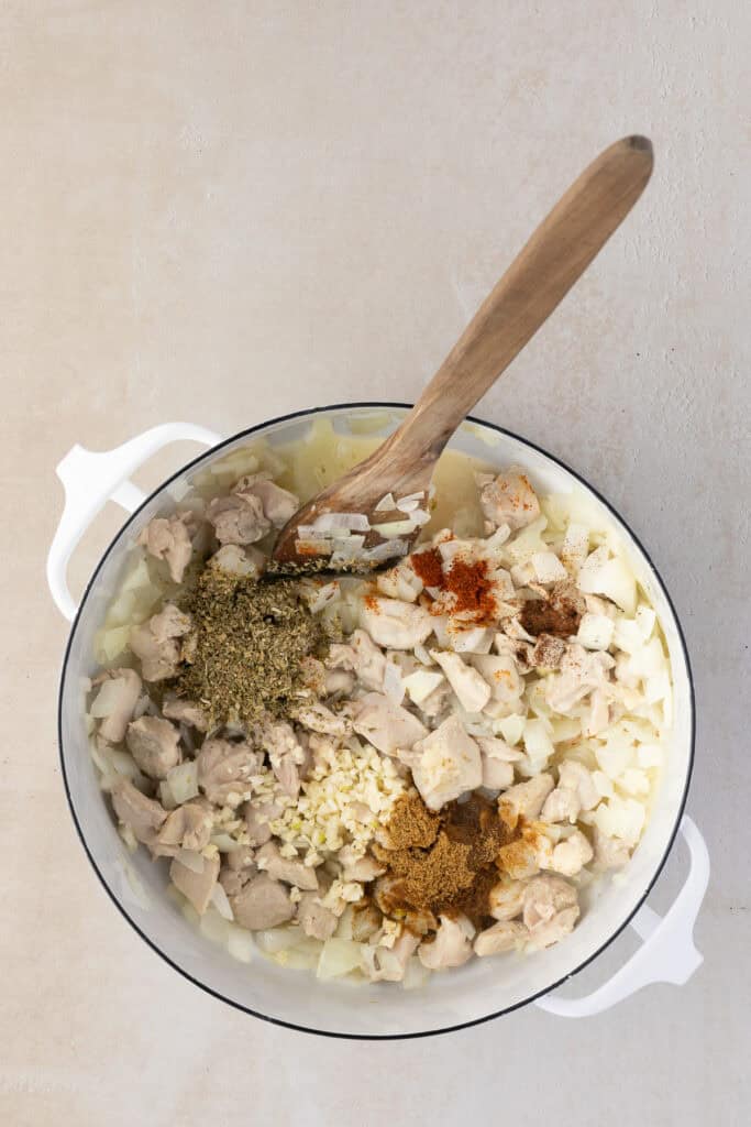 Cumin, cloves, cayenne and oregano, green chiles, garlic added to pot of onion and chicken.