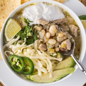 Bowl of white bean and chicken chili garnished with cheese, avocado, jalape&ntilde;o, cilantro, sour cream and lime.